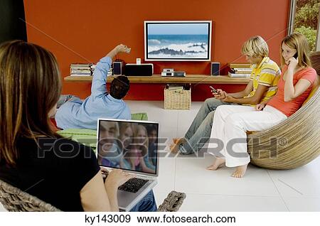 Family in living room, woman using laptop, man watching TV, 2 teens using mobile phone View Large Photo Image Stock Photo - Family in living room, woman using laptop, man watching TV, 2 teens using mobile phone. Fotosearch
