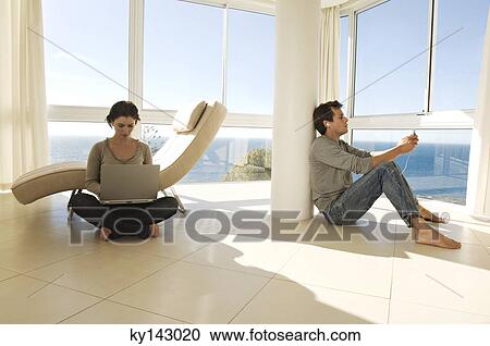 Young couple in living-room, woman using laptop and man listening to MP3 player View Large Photo Image Stock Image - Young couple in living-room, woman using laptop and man listening to MP3 player. Fotosearch