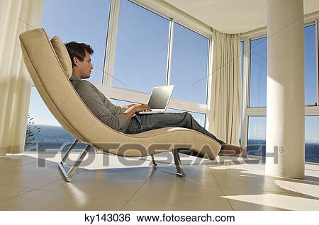 Stock Photograph - Young man using laptop in armchair. Fotosearch