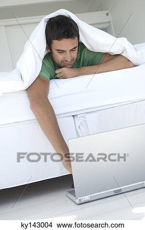 Young man using laptop in bed View Large Photo Image Picture - Young man using laptop in bed. Fotosearch