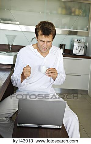 Young man using laptop in kitchen View Large Photo Image Stock Image - Young man using laptop in kitchen. Fotosearch