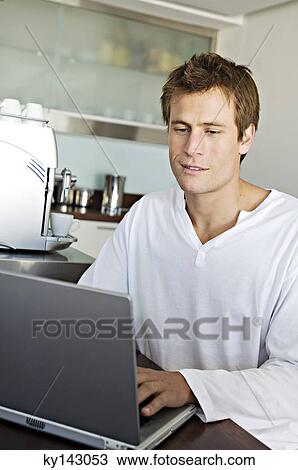 Young man using laptop in kitchen View Large Photo Image Stock Image - Young man using laptop in kitchen. Fotosearch