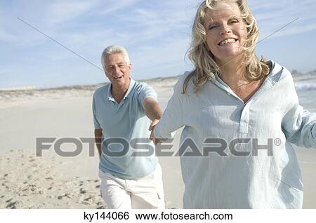 Couple holding hands, walking on the beach View Large Photo Image Stock Photograph - Couple holding hands, walking on the beach. Fotosearch