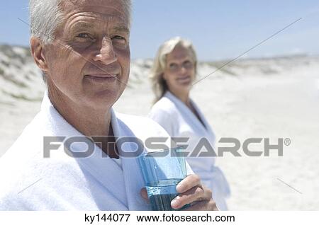 Couple in bathrobe on the beach, man with glass of water in foreground View Large Photo Image Stock Photo - Couple in bathrobe on the beach, man with glass of water in foreground. Fotosearch