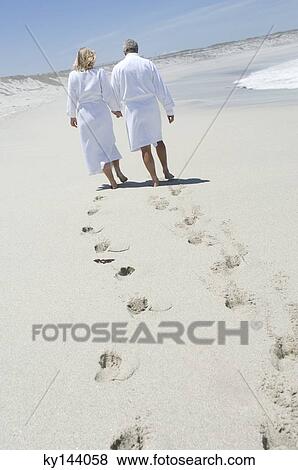 Stock Photo - Couple in bathrobe walking on the beach, rear view. Fotosearch
