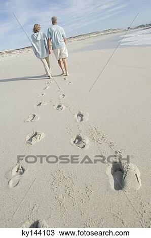Stock Image - Couple walking on the beach, rear view. Fotosearch