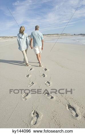 Couple walking on the beach, rear view View Large Photo Image Stock Photograph - Couple walking on the beach, rear view. Fotosearch