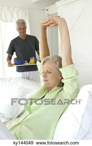 Man bringing breakfast to woman stretching in bed View Large Photo Image Stock Photo - Man bringing breakfast to woman stretching in bed. Fotosearch