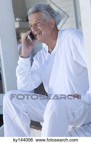 Stock Photograph - Man using mobile phone sitting on wooden terrace. Fotosearch