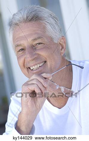 Stock Photo - Portrait of smiling man, holding eyeglasses. Fotosearch