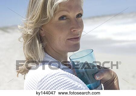 Stock Photo - Portrait of thinking woman on the beach, holding glass of water. Fotosearch