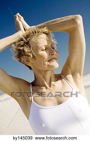 Stock Photo - Senior woman doing yoga on the beach. Fotosearch