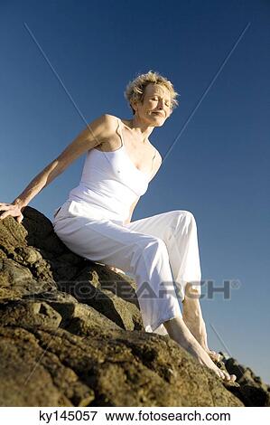 Stock Photo - Senior woman sitting on seaside rocks. Fotosearch