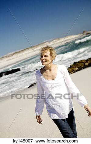 Senior woman walking on beach View Large Photo Image Stock Photo - Senior woman walking on beach. Fotosearch
