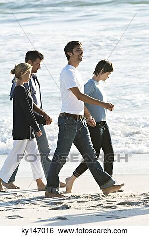 Stock Photograph - 2 couples holding hands, walking on the beach. Fotosearch