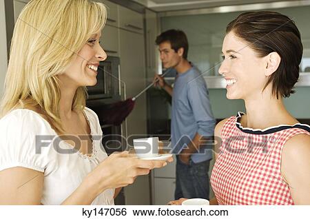 2 smiling women talking, man using feather duster in background View Large Photo Image Stock Photograph - 2 smiling women talking, man using feather duster in background. Fotosearch