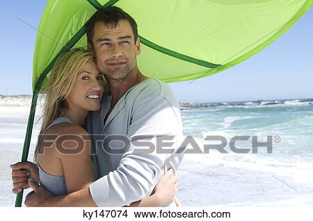 Couple embracing on the beach, beach umbrella View Large Photo Image Picture - Couple embracing on the beach, beach umbrella. Fotosearch