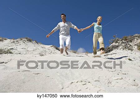 Couple holding hands, running down sand dune View Large Photo Image Stock Image - Couple holding hands, running down sand dune. Fotosearch