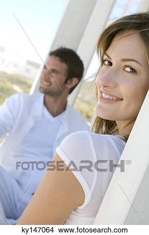 Couple on terrace, woman smiling for the camera in foreground View Large Photo Image Picture - Couple on terrace, woman smiling for the camera in foreground. Fotosearch