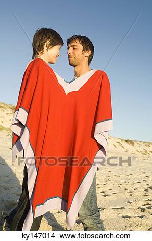 Couple on the beach, sharing a poncho View Large Photo Image Picture - Couple on the beach, sharing a poncho. Fotosearch