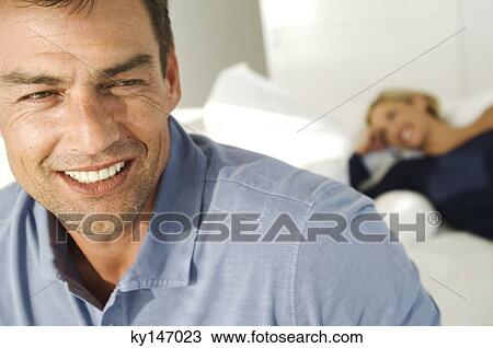 Portrait of smiling man, woman lying on bed in background View Large Photo Image Stock Image - Portrait of smiling man, woman lying on bed in background. Fotosearch