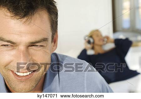 Stock Image - Portrait of smiling man, woman listening to music in background. Fotosearch