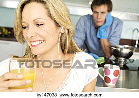 Stock Photo - Portrait of young smiling woman holding glass of orange juice, tired man in background. Fotosearch