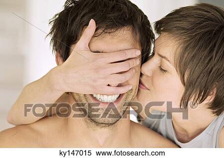 Stock Photography - Portrait of young woman kissing man, covering his eyes. Fotosearch