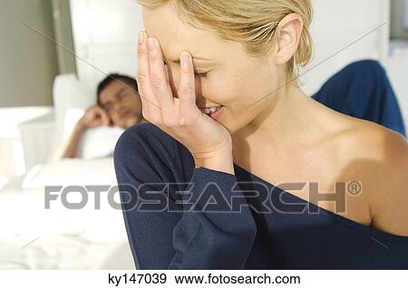 Portrait of young woman laughing, hand covering mouth, sulking man lying in bed in background View Large Photo Image Stock Photo - Portrait of young woman laughing, hand covering mouth, sulking man lying in bed in background. Fotosearch