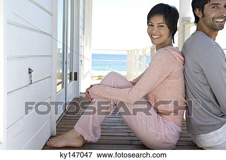 Smiling couple sitting, back to back, on wooden terrace View Large Photo Image Stock Photo - Smiling couple sitting, back to back, on wooden terrace. Fotosearch