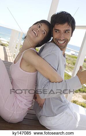 Smiling couple sitting, back to back, on wooden terrace View Large Photo Image Stock Photography - Smiling couple sitting, back to back, on wooden terrace. Fotosearch