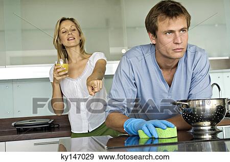 Stock Photo - Smiling woman pointing at angry man holding sponge. Fotosearch