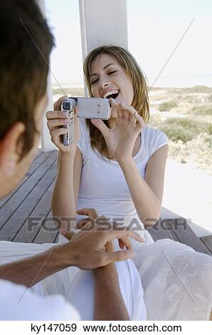 Young woman filming man with camcorder on wooden terrace View Large Photo Image Stock Photo - Young woman filming man with camcorder on wooden terrace. Fotosearch