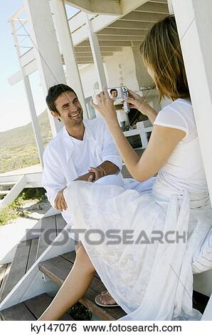 Young woman filming man with camcorder on wooden terrace View Large Photo Image Stock Photograph - Young woman filming man with camcorder on wooden terrace. Fotosearch