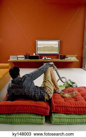 Man watching TV lying on cushions, vacuum cleaner in front of him View Large Photo Image Stock Image - Man watching TV lying on cushions, vacuum cleaner in front of him. Fotosearch