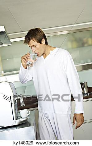 Stock Photo - Young man drinking water in kitchen. Fotosearch
