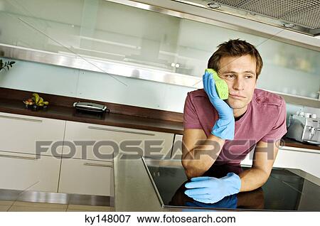 Young man in kitchen, leaning sponge against his cheek View Large Photo Image Stock Photo - Young man in kitchen, leaning sponge against his cheek. Fotosearch