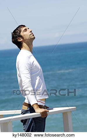 Young man leaning against balustrade, eyes closed, sea in background View Large Photo Image Stock Image - Young man leaning against balustrade, eyes closed, sea in background. Fotosearch