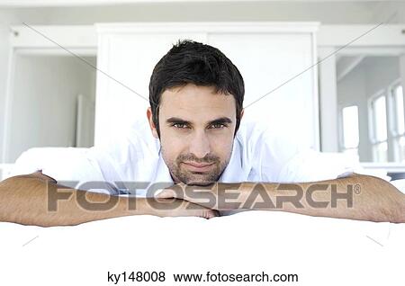 Stock Photo - Young man lying on bed, looking at camera. Fotosearch
