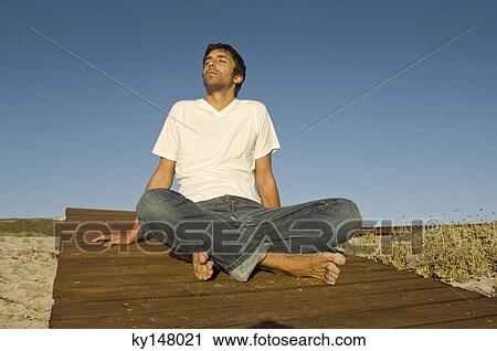 Young man sitting cross-legged, outdoors View Large Photo Image Stock Image - Young man sitting cross-legged, outdoors. Fotosearch