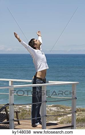 Stock Photo - Young man stretching on terrace, sea in background. Fotosearch