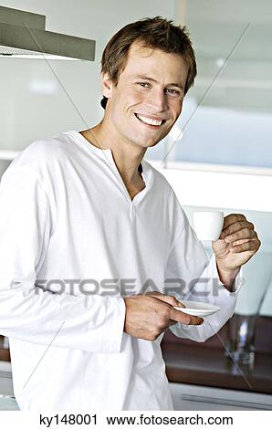 Young smiling man in kitchen, holding coffee cup View Large Photo Image Stock Image - Young smiling man in kitchen, holding coffee cup. Fotosearch