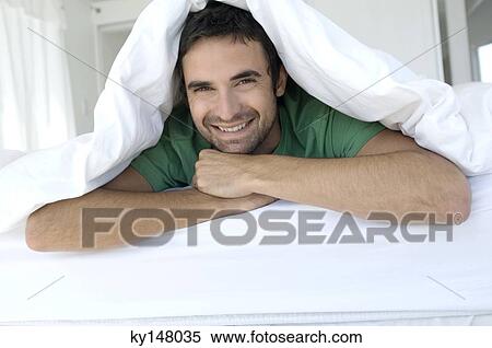 Young smiling man lying under duvet View Large Photo Image Stock Photography - Young smiling man lying under duvet. Fotosearch