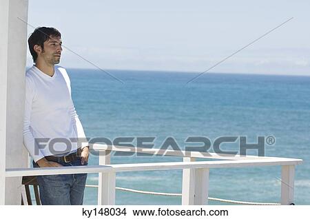 Young thinking man leaning against wall on a terrace, sea in background View Large Photo Image Picture - Young thinking man leaning against wall on a terrace, sea in background. Fotosearch