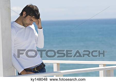 Young thinking man leaning against wall on a terrace, sea in background View Large Photo Image Stock Photo - Young thinking man leaning against wall on a terrace, sea in background. Fotosearch