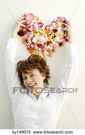 Stock Photography - Portrait of young smiling woman holding flowers petals in heart shape. Fotosearch