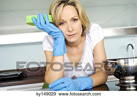 Young woman in kitchen holding sponge, looking tired View Large Photo Image Stock Photo - Young woman in kitchen holding sponge, looking tired. Fotosearch