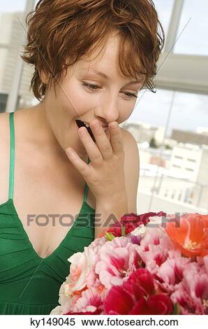 Stock Photography - Young woman looking at bunch of flowers, hand covering mouth. Fotosearch