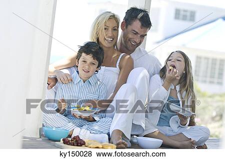 Couple and two children eating, sitting on wooden terrace View Large Photo Image Stock Photo - Couple and two children eating, sitting on wooden terrace. Fotosearch
