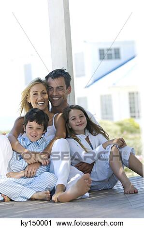 Couple and two children smiling for the camera, sitting on wooden terrace View Large Photo Image Stock Image - Couple and two children smiling for the camera, sitting on wooden terrace. Fotosearch